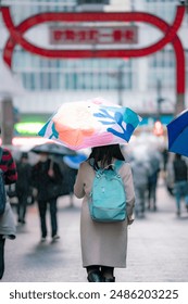 Unrecognizable young Latina woman strolls down a rainy street in Shinjuku, Tokyo, Japan, holding an umbrella and looking calm.