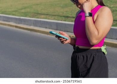 Unrecognizable Young Latina woman using smartphone while adjusting earbuds on the street - Powered by Shutterstock