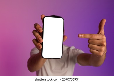 Unrecognizable Young Man Holding Smartphone In Front Of His Face, Pointing At Empty Screen, Offering Space For Mobile App Or Website, Demonstrating Mockup For Online Ad In Neon Light, Selective Focus