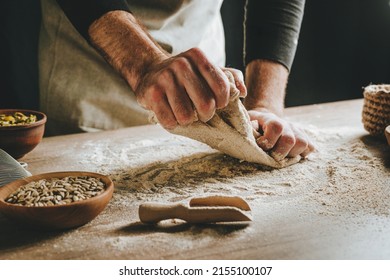 Unrecognizable young man kneading dough on wooden table. Males hands making bread on dark background. Selective focus. - Powered by Shutterstock