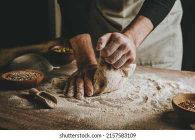 Unrecognizable young man kneading dough on wooden table. Males hands making bread on dark background. Selective focus. - Powered by Shutterstock