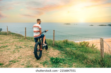 Unrecognizable young man riding a fat bike looking at the beach from the coast