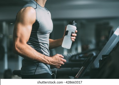 Unrecognizable young man in sportswear running on treadmill at gym and holding bottle of water  - Powered by Shutterstock