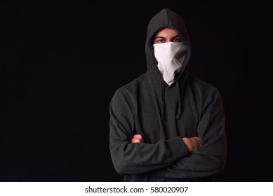Unrecognizable young man wearing white balaclava and black hoodie ready to protest at a rally on a dark background