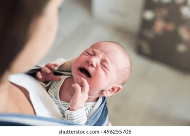 Unrecognizable young mother with her crying son in sling