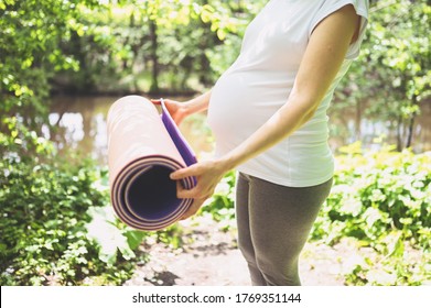 Unrecognizable young pregnant woman preparing to do yoga exercising with pink yoga mat. Active future mother sport lifestyle. Healthy pregnancy concept.