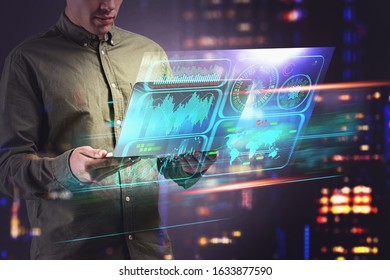 Unrecognizable young programmer using laptop over blurry cityscape background with double exposure of futuristic HUD infographics interface. Toned image
