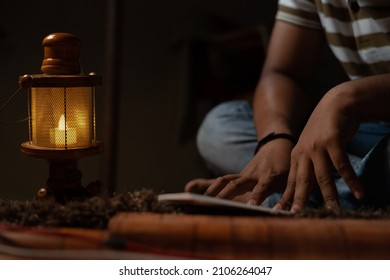 unrecognizable Young student busy reading during night under oil lamp or lantern due to power loss and Poverty - concpet of power cut, blackout, electricity failure during examination.