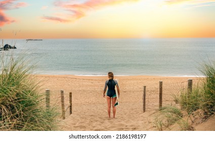 Unrecognizable Young Surfer Woman With Wetsuit And Surfboard Looking At The Sea From The Sand