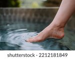 Unrecognizable young woman is dipping her foot in cool water of pond, refreshing and hardening concept.