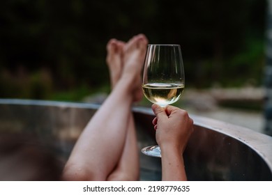 Unrecognizable young woman with feet up relaxing with glass of wine in hot tub outdoor in nature. - Powered by Shutterstock