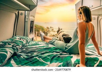 Unrecognizable young woman with her boston terrier dog watching the sunset sitting on the bed of her camper van - Powered by Shutterstock