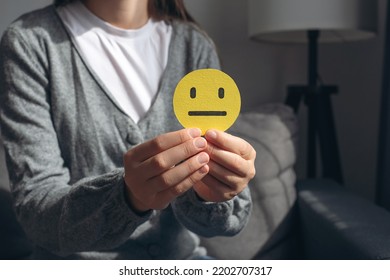 Unrecognizable Young Woman Holding Small Yellow Sad Face, Demonstrate Bad Emoticon Sitting On Grey Couch. Feedback Rating And Positive Customer Review, Experience, Satisfaction Survey Concept