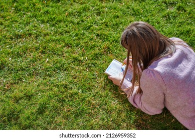 Unrecognizable Young Woman Kills Time Playing With A Word Search Puzzle Lying On The Lawn In The Backyard Of Her Home On A Sunny Spring Day.