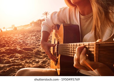 unrecognizable young woman playing guitar at sunset at the beach in a summer day - Powered by Shutterstock