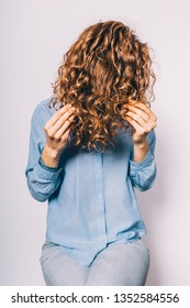 Unrecognizable Young Woman Wearing Blue Shirt Applying Cosmetic Care Product On Her Curly Hair Tips.