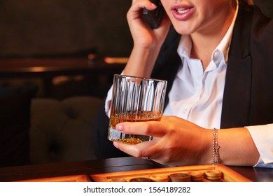 Unrecognizable Young Woman In White Blouse And Suit Drinking Whiskey And Talking By Phone In Bar. Business Woman Resting After Hard Day.