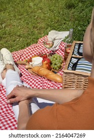 Unrecognizable Young Woman In White Pants Outside Having Picnic, Eating And Playing Guitar. Summer Fun And Leisure