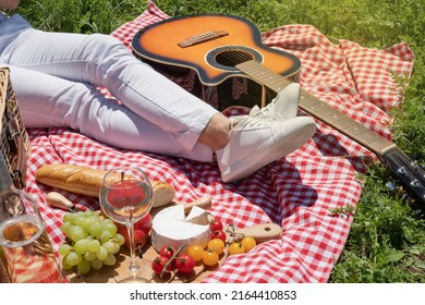 Unrecognizable Young Woman In White Pants Outside Having Picnic, Eating And Playing Guitar. Summer Fun And Leisure