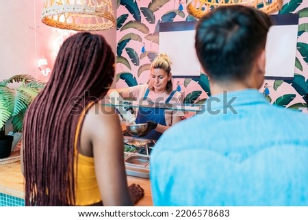 Unrecognized african american woman and her friend buying a poke bowl in a cool restaurant.