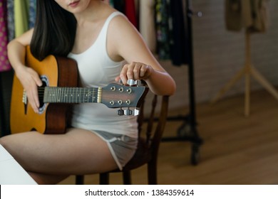 Unrecognized Asian Woman Singer Hands Tunes A Six Stringed Guitar In Backstage Sitting. Causal Girl Musician Performer Tone Tuning On Instrument In Dressing Room Preparing For Singing Progress Show.