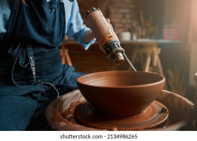 Unrecognized female artisan with blowtorch in hand working with fresh wet clay tableware in pottery workshop - Powered by Shutterstock