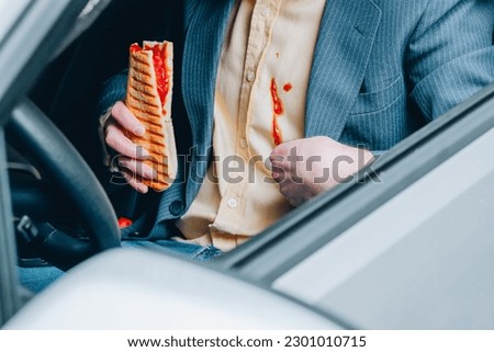 An unrecognized man showing a dirty sauce stain on his shirt, in the other hand he holding hot dog in car. Eating while driving. daily life stain concept. High quality photo