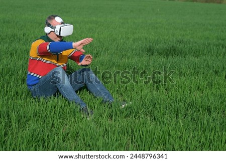 Unrecognized man sitting on green grass and touching the air during the VR experience. Digital agriculture business. outdoors. High quality photo