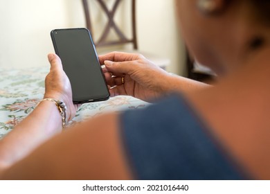 Unrecognized Old Woman At Home Using A Mobile Phone With Black Screen. Mockup Device To Add Elements.