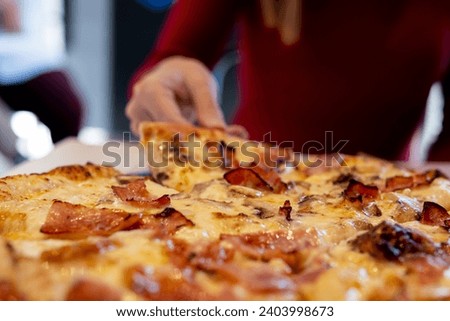 Unrecognized woman in red sweater, eagerly grabbing a fresh, hot pizza slice.