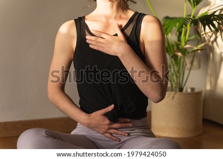 Unrecognized woman wearing sports clothes practicing yoga at home and breathing slowly.