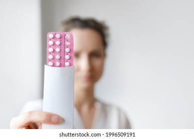 Unrecognized woman in white blouse holding hormonal oral contraceptives in a pink blister. Concept of Hormonal methods of birth control. Estrogen and Progestin hormonal balance.