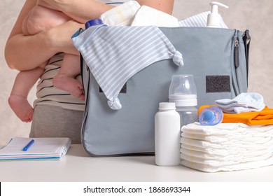 Unrecognizible Caucasian Woman Packing Big Blue Diaper Bag For A Walk Or Small Trip With Infant Baby. Diapers, Nappy, Hat, Bottle And Other Necessary Things For Journey With Baby.