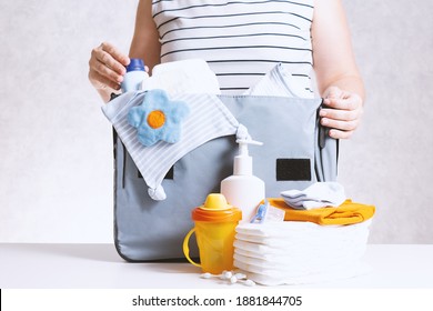 Unrecognizible Pregnant Caucasian Woman In Striped T-shirt Packing Big Gray Diaper Bag To Maternity Hospital. Diapers, Bottle And Other Necessary Things For Newborn Baby.