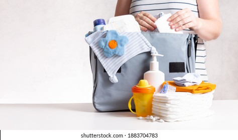 Unrecognizible Pregnant Caucasian Woman In Striped T-shirt Packing Big Gray Diaper Bag To Maternity Hospital. Diapers, Bottle And Other Necessary Things For Newborn Baby. Copy Space.