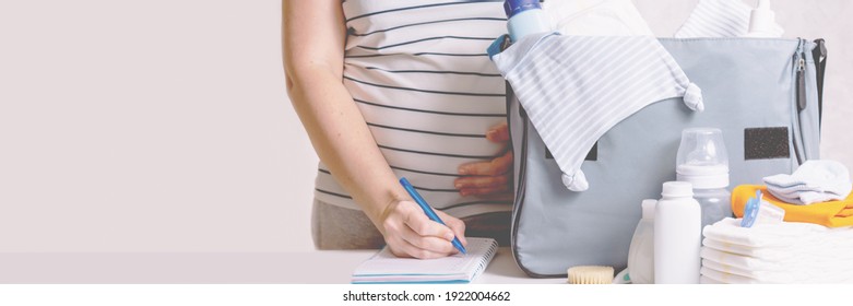 Unrecognizible Pregnant Caucasian Woman In Striped T-shirt Packing Big Blue Diaper Bag To Maternity Hospital. Diapers, Nappy, Hat, Bottle And Other Necessary Things For Newborn Baby. Banner. 