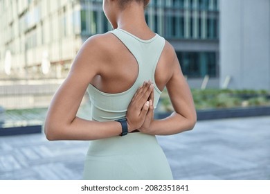 Unrecongizable fit woman practices yoga does reverse prayer pose clasps hands behind back dressed in comfortable activewear poses outdoors in urban setting stretches arms. Daily practice concept