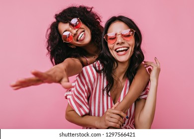 Unrestrained merriment of two girls captured on snapshot. Photos in pink shades of brunettes with beautiful curls, embracing in friendly way - Shutterstock ID 1297566421