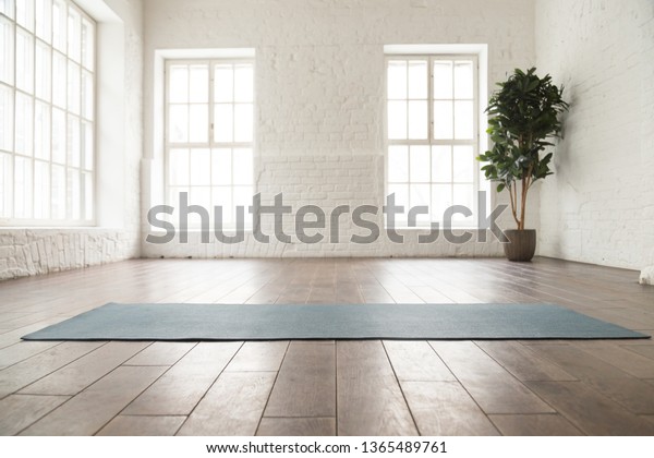 Unrolled yoga\
mat on wooden floor in modern fitness center or at home with big\
windows and white brick walls, comfortable space for doing sport\
exercises, meditating, yoga\
equipment