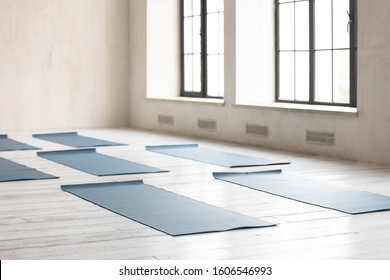 Unrolled yoga mats on wooden floor in fitness center with nobody, modern class prepared for group working out, comfortable space for doing sport exercises, empty class room with big windows