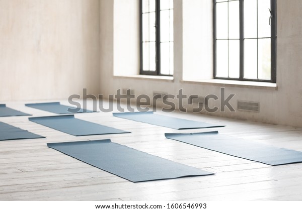 Unrolled yoga mats on wooden floor in fitness\
center with nobody, modern class prepared for group working out,\
comfortable space for doing sport exercises, empty class room with\
big windows