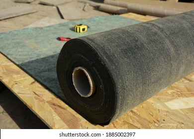Unrolling waterproofing, water-resistant felt, bituminous roofing underlayment on the roof sheathing, roof deck before asphalt shingles installation while roofing construction.  - Shutterstock ID 1885002397
