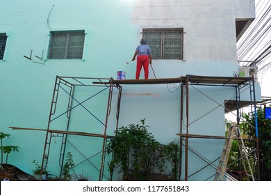 Unsafe condition concept, A painter woman standing on a scaffolding. She painting the blue color at the wall of house. She does not wear protective equipment.