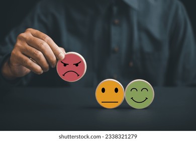 Unsatisfied customer holding frown icon on wooden circle. Conceptual representation of customer satisfaction evaluation, depicting bad experience, negative review, and low score.