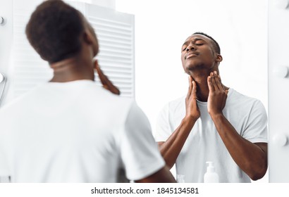 Unshaven Black Man Touching Neck With Bristle And Stubble Before Shaving Face Standing Near Mirror In Bathroom At Home. Male Facial Skincare, Morning Beauty And Self-Care Routine. Selective Focus - Powered by Shutterstock