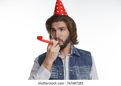 Unshaven Young Male Celebrating Success, Wearing Red Cone Hat And Blowing Party Horn, Having Excited Happy Cheerful Expression On His Hairy Face. People, Joy, Celebration, Rest And Relaxation