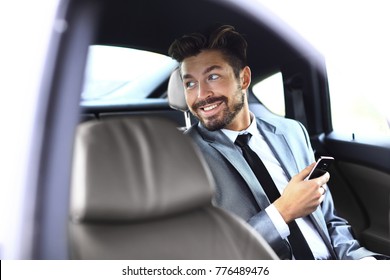 Unsmiling Businessman Sitting In The Back Seat In His Car