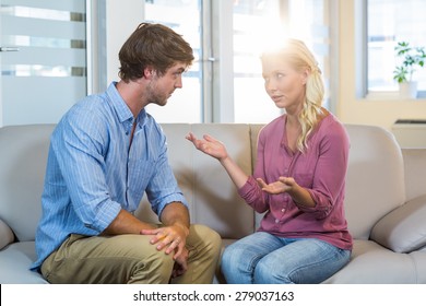 Unsmiling couple talking to each other in the therapist office