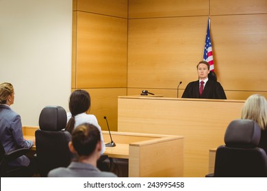 Unsmiling Judge With American Flag Behind Him In The Court Room