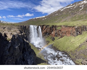 unspoiled landscape of the Icelandic east fjords with an impressive waterfall cascading down rocky cliffs and a rainbow in the spray - Powered by Shutterstock